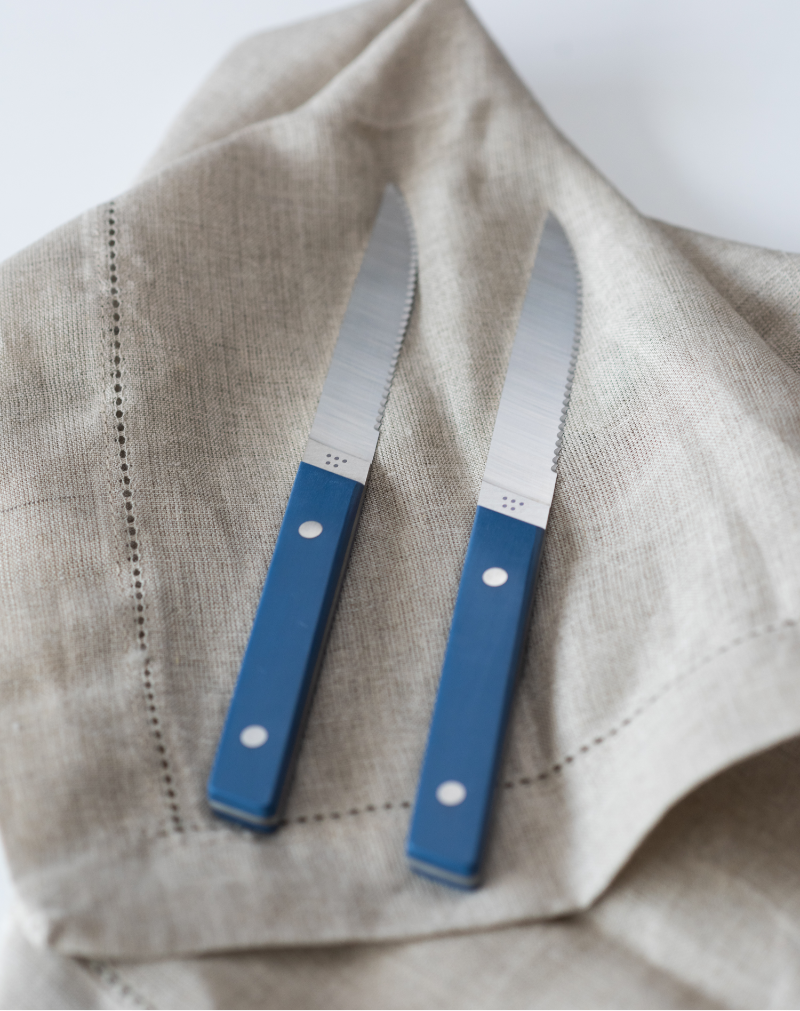 Two Blue Misen Steak Knives seen from above, resting atop a beige linen cloth.