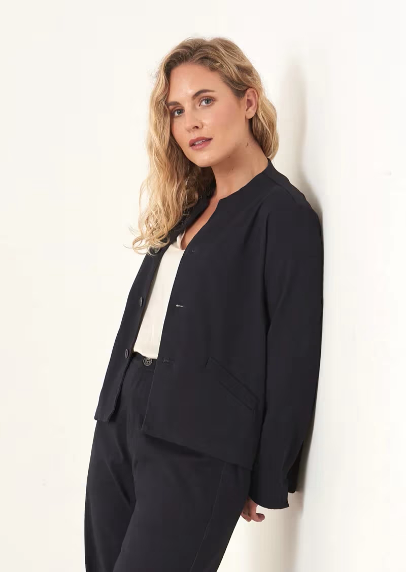 A model wearing a blue-black boxy jacket over a white top and matching trousers
