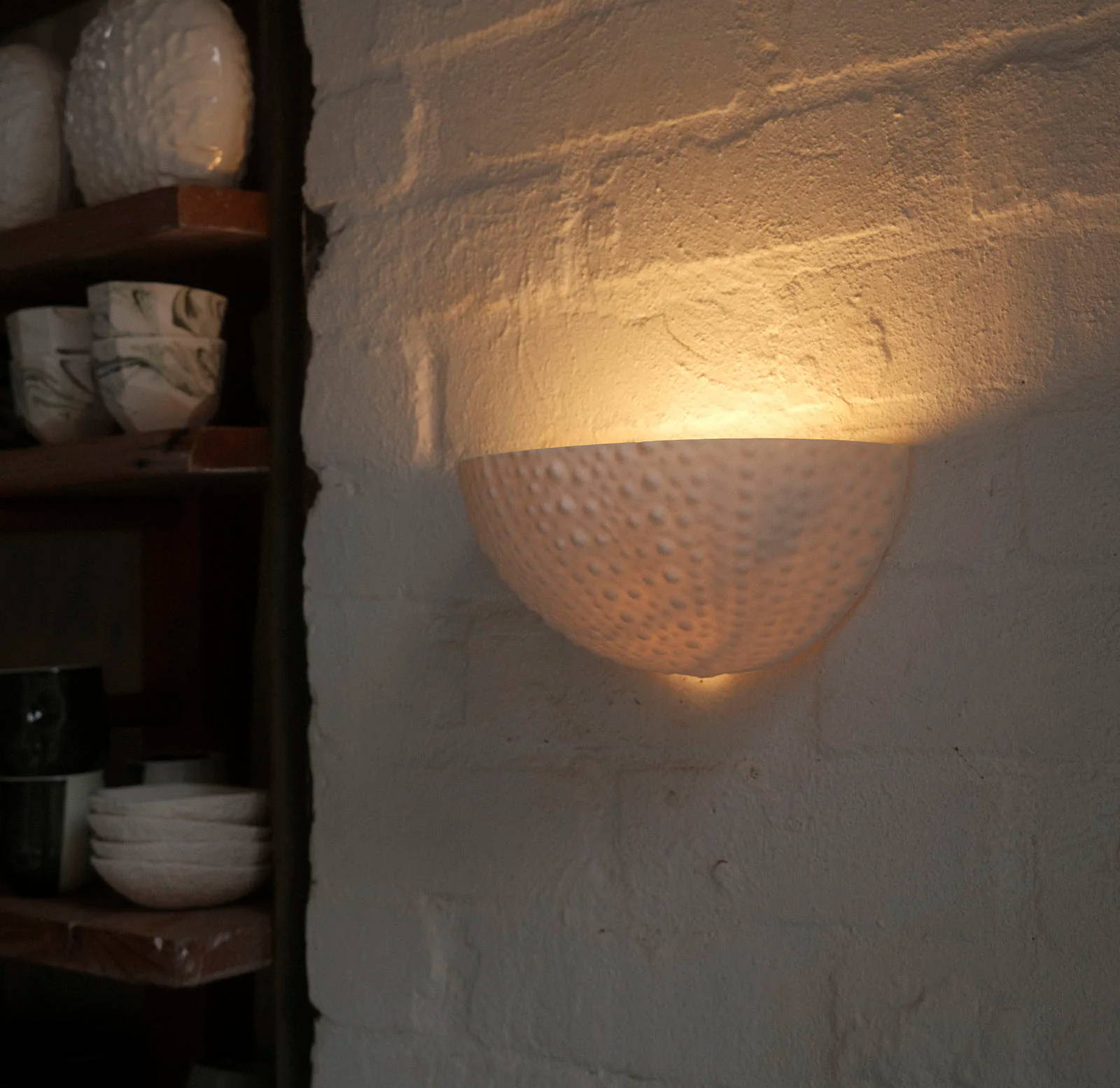 Urchin wall sconce casting a warm glow on a white brick wall.