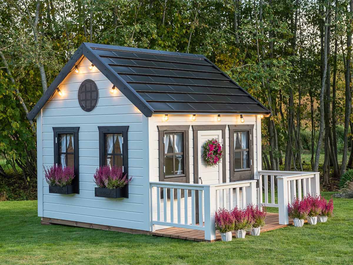 White and Black Outdoor Playhouse decorated with flowers in a backyard by WholeWoodPlayhouses