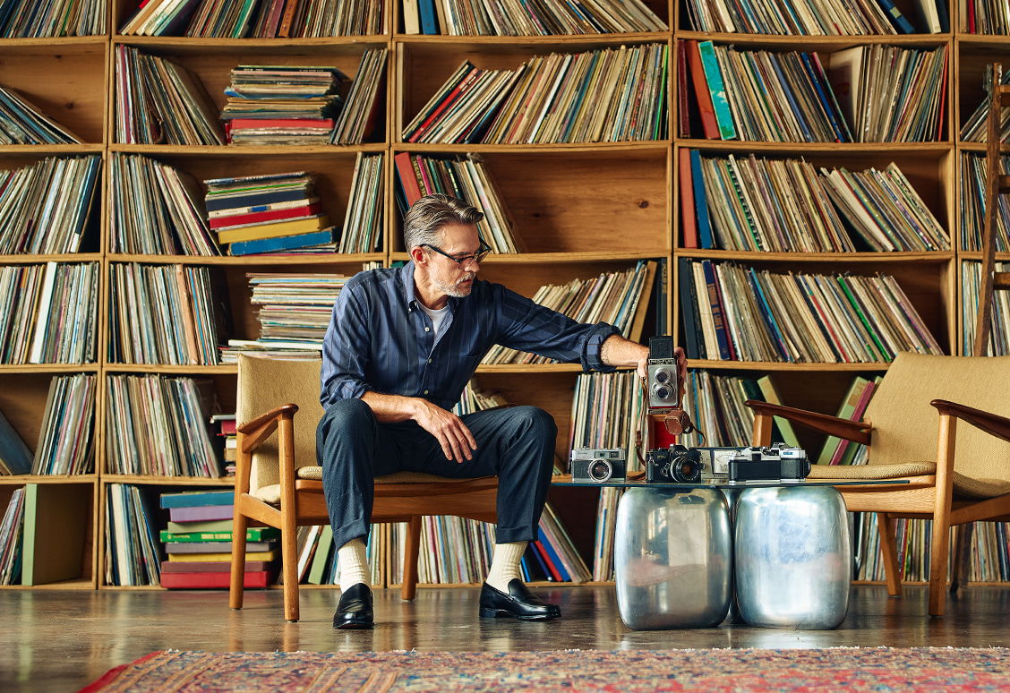 Person sitting with vinyl records and chairs in a cozy library setting.