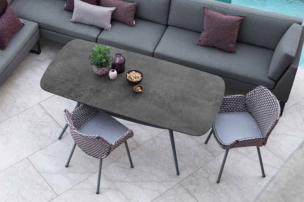 A slate grey dining table with table height sofa and woven chairs.