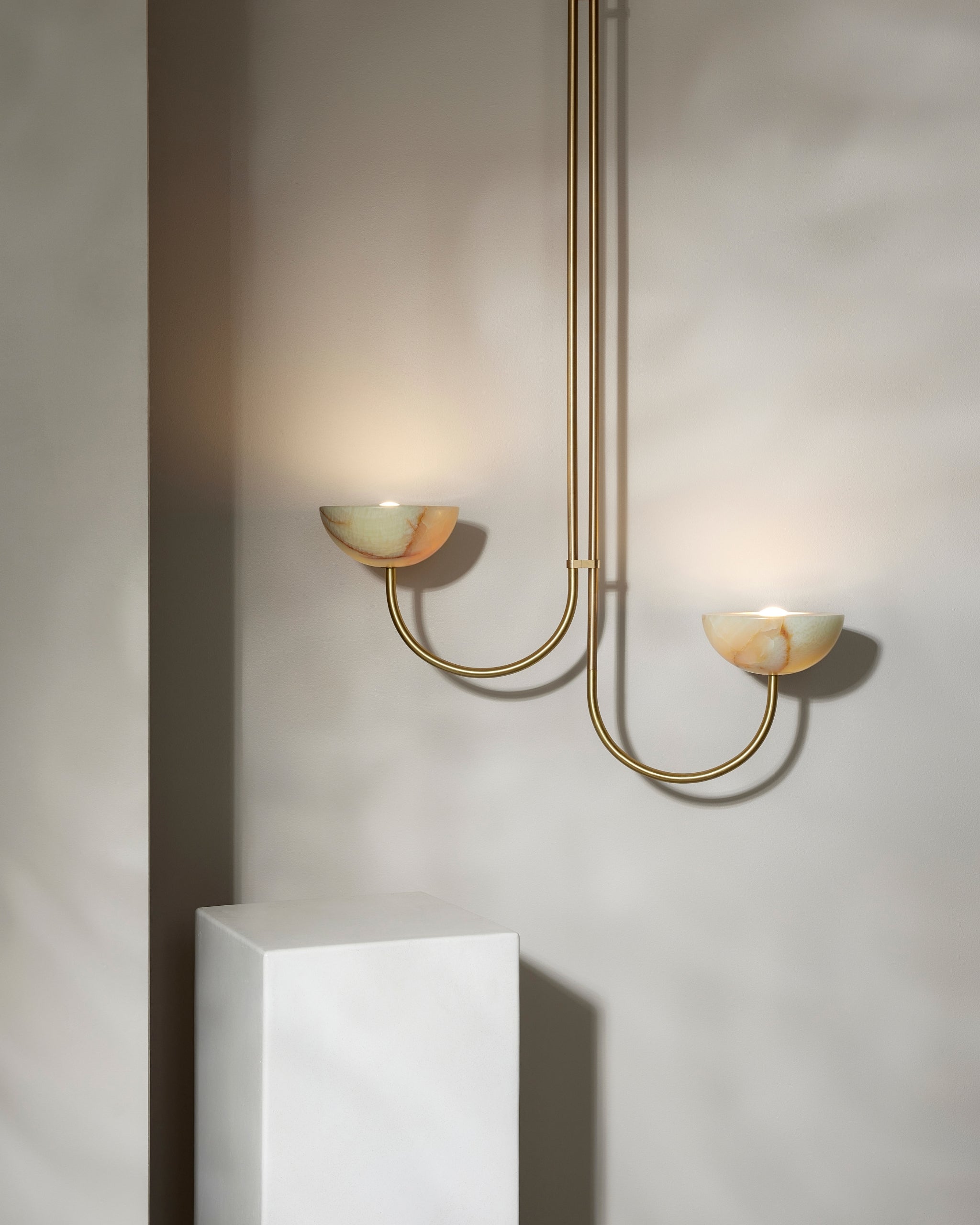 Modern pendant with gold finish and two light bulbs on a neutral wall.