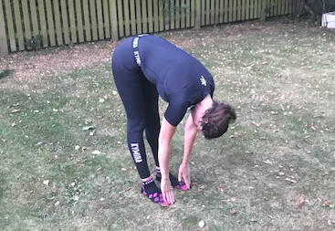 A woman standing up, bent over, with her hands touching her toes. 