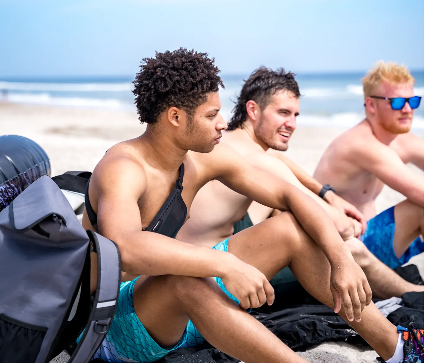 Friends hanging out on the beach with waterproof pocket shorts and auto sealing dry bags. 