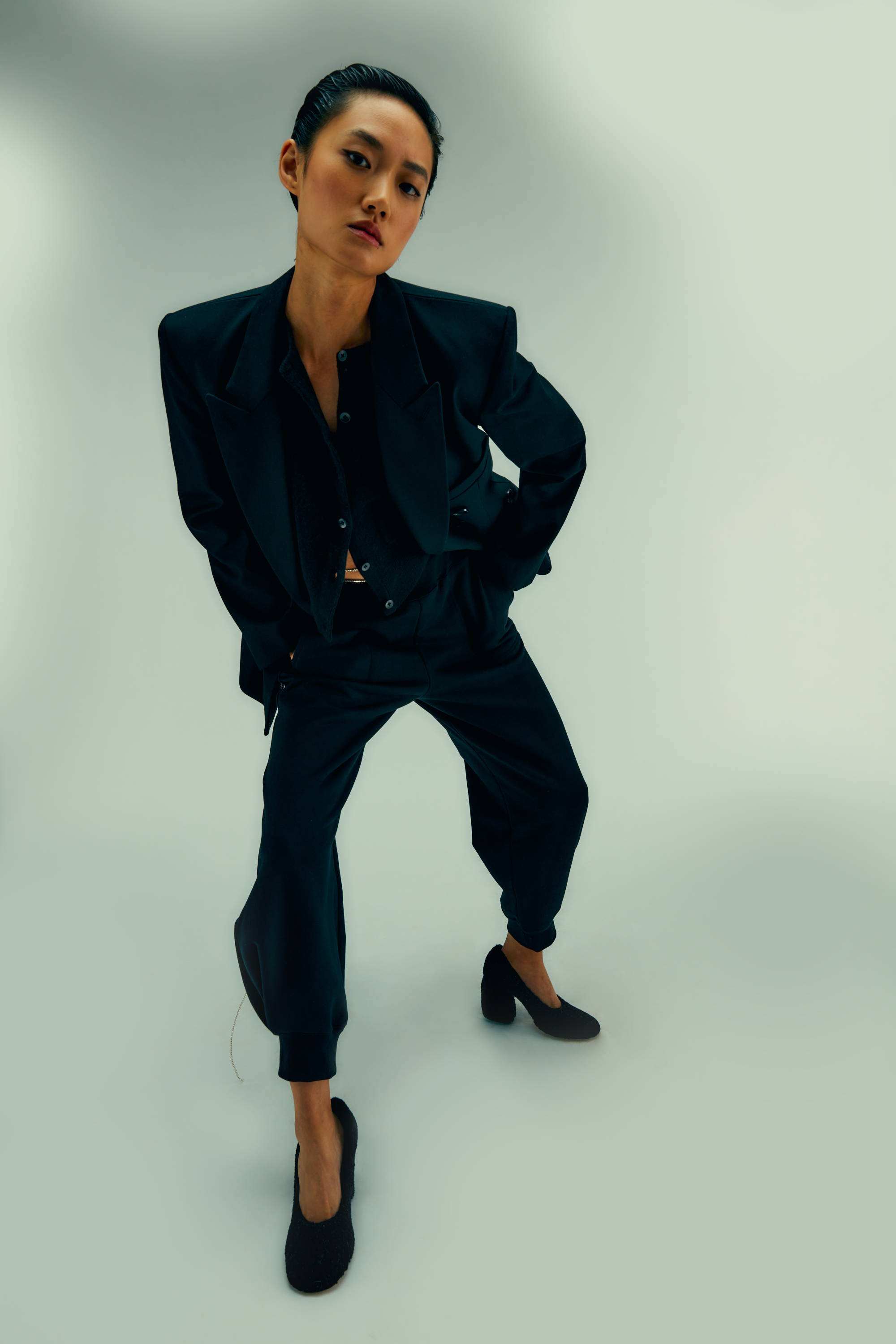A person in a stylish black suit, posing confidently against a light background.