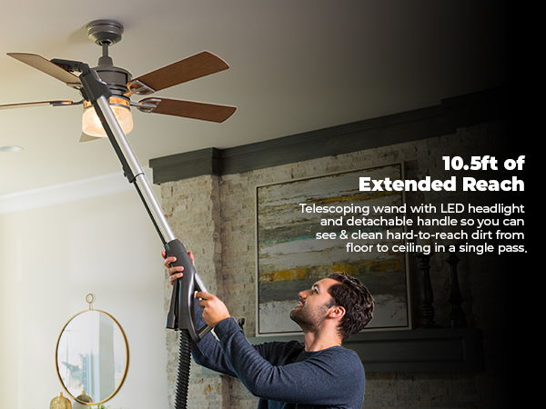 Person using a vacuum cleaner attachment to clean a ceiling fan.