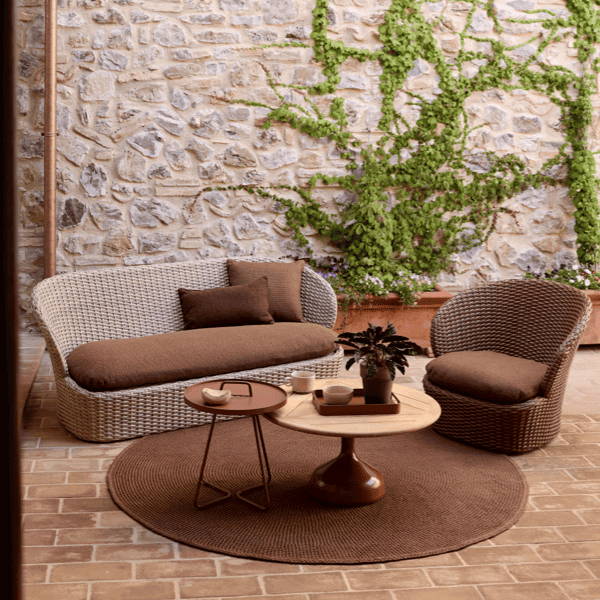 Coast Loveseat with a curved woven frame and brown cushions, styled in a rustic courtyard with terracotta accents, perfect for cozy outdoor lounging in natural, timeless settings.