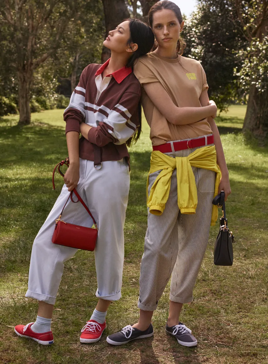 Two women posing outdoors in casual outfits and sneakers.