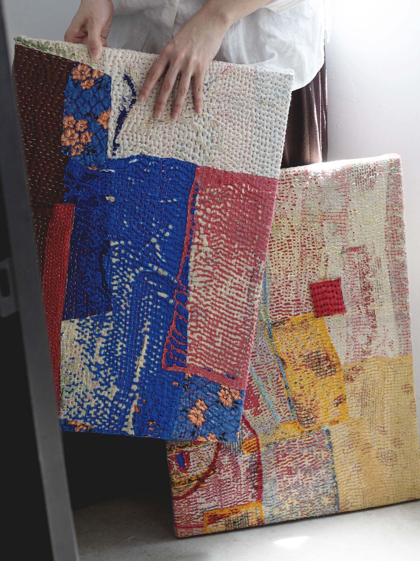 Person holding colorful patchwork fabric pieces against a neutral background.
