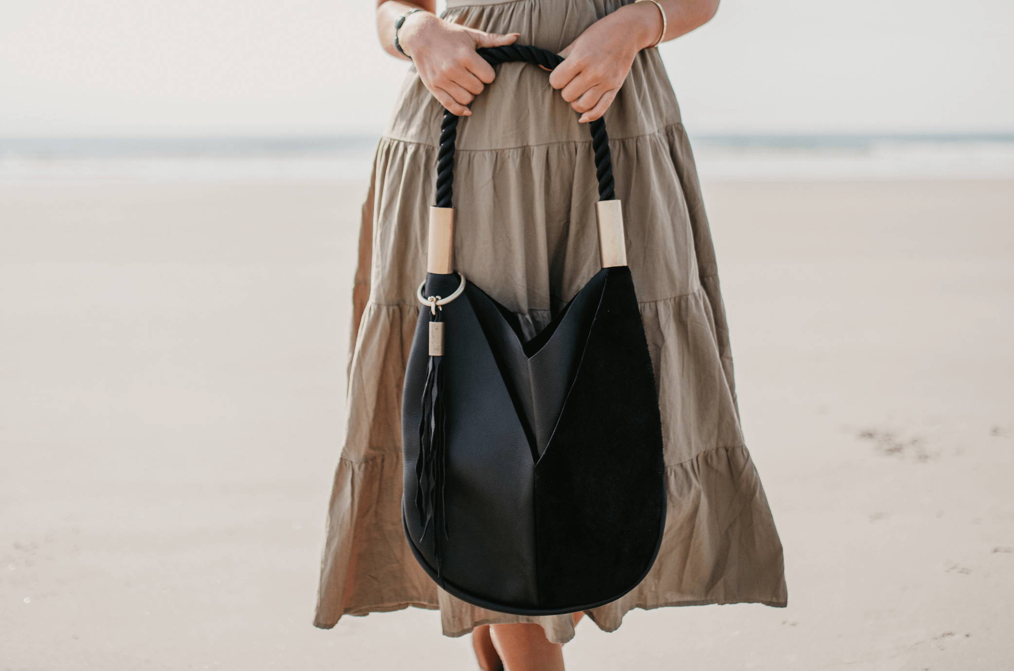 Black leather tote bag with seaweed tassel on the beach