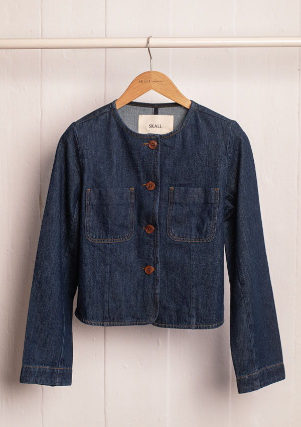 Denim jacket with buttons and two front pockets hanging on a wooden hanger.