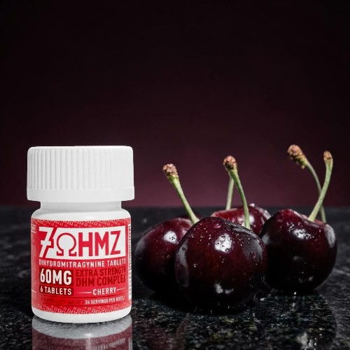 Bottle of gummies next to fresh cherries on a dark surface.