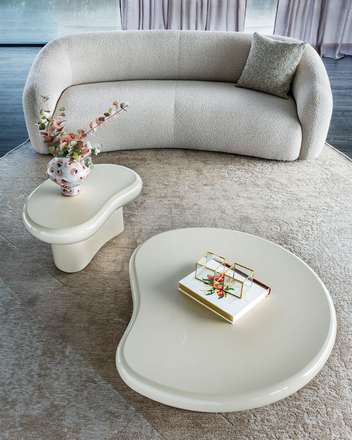 Modern living room with curved sofa, unique coffee tables, and decorative vase.