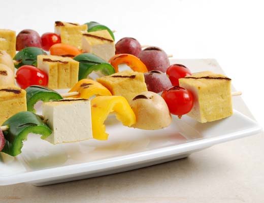 Colorful vegetable and cheese skewers arranged on a white plate.