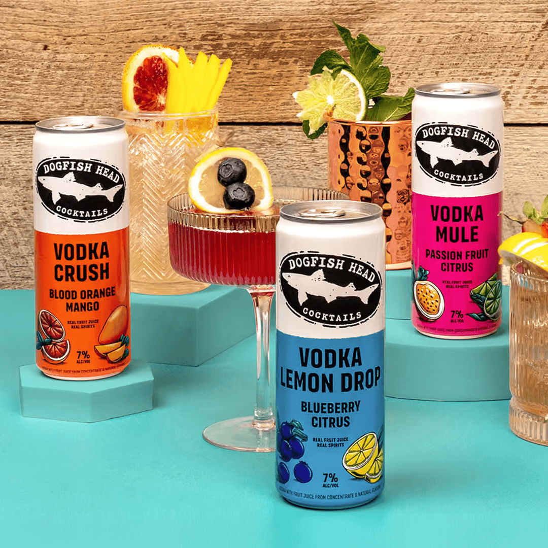 Cans of flavored vodka drinks with garnished cocktails on a colorful table.