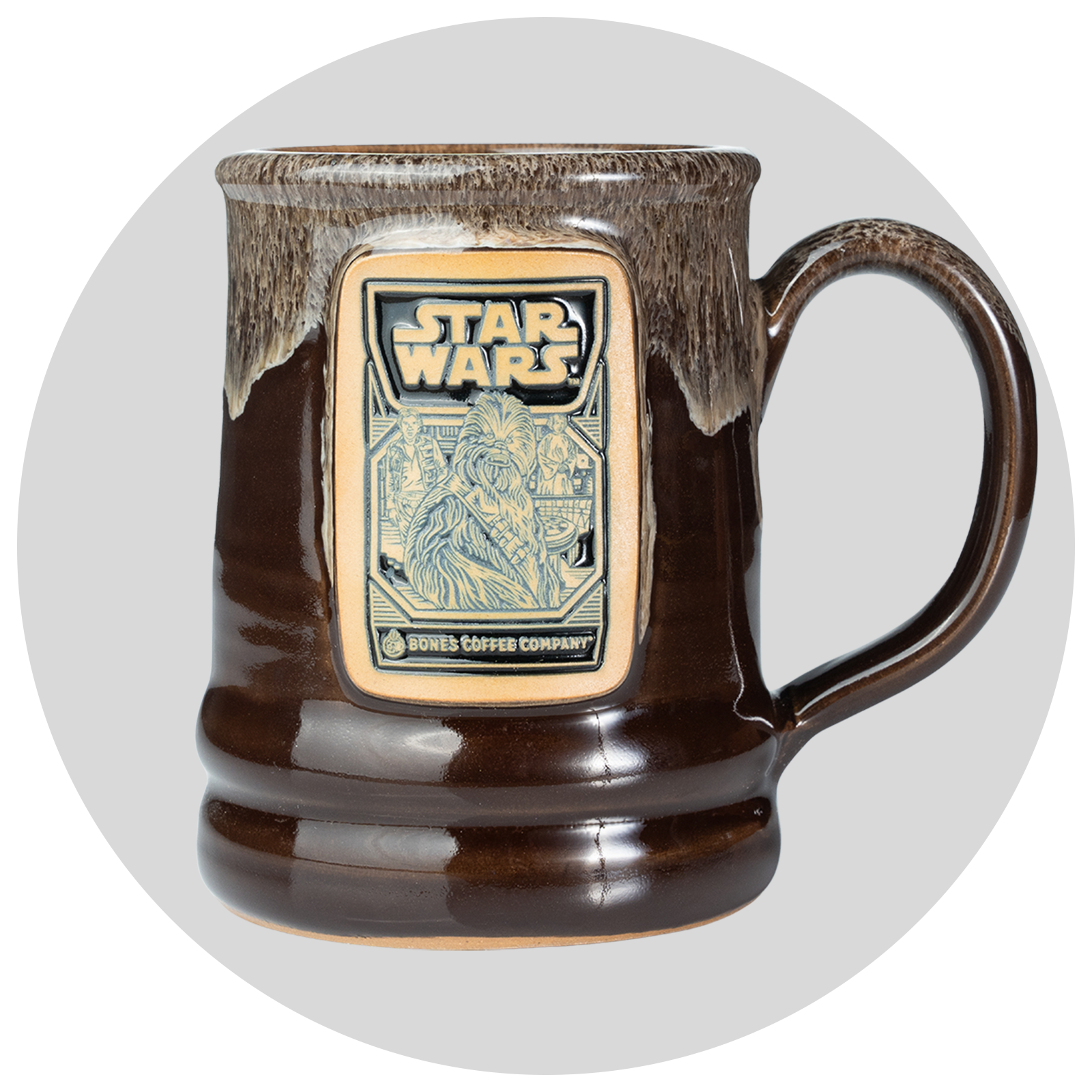 The front of the Bones Coffee Company Wookiee Cookie Hand Thrown Mug. It's colored chocolate with a sand-white glaze on top of it. The golden medallion has the Wookiee Cookie art on it. Behind it is a gray circle.