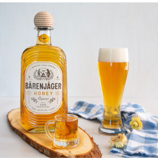 Bottle of Barenjager honey liqueur with a glass and beer on a wooden surface.
