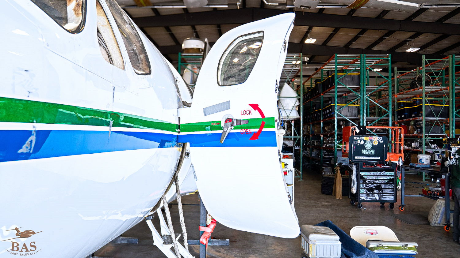 Aircraft in hangar with open door and maintenance equipment visible.