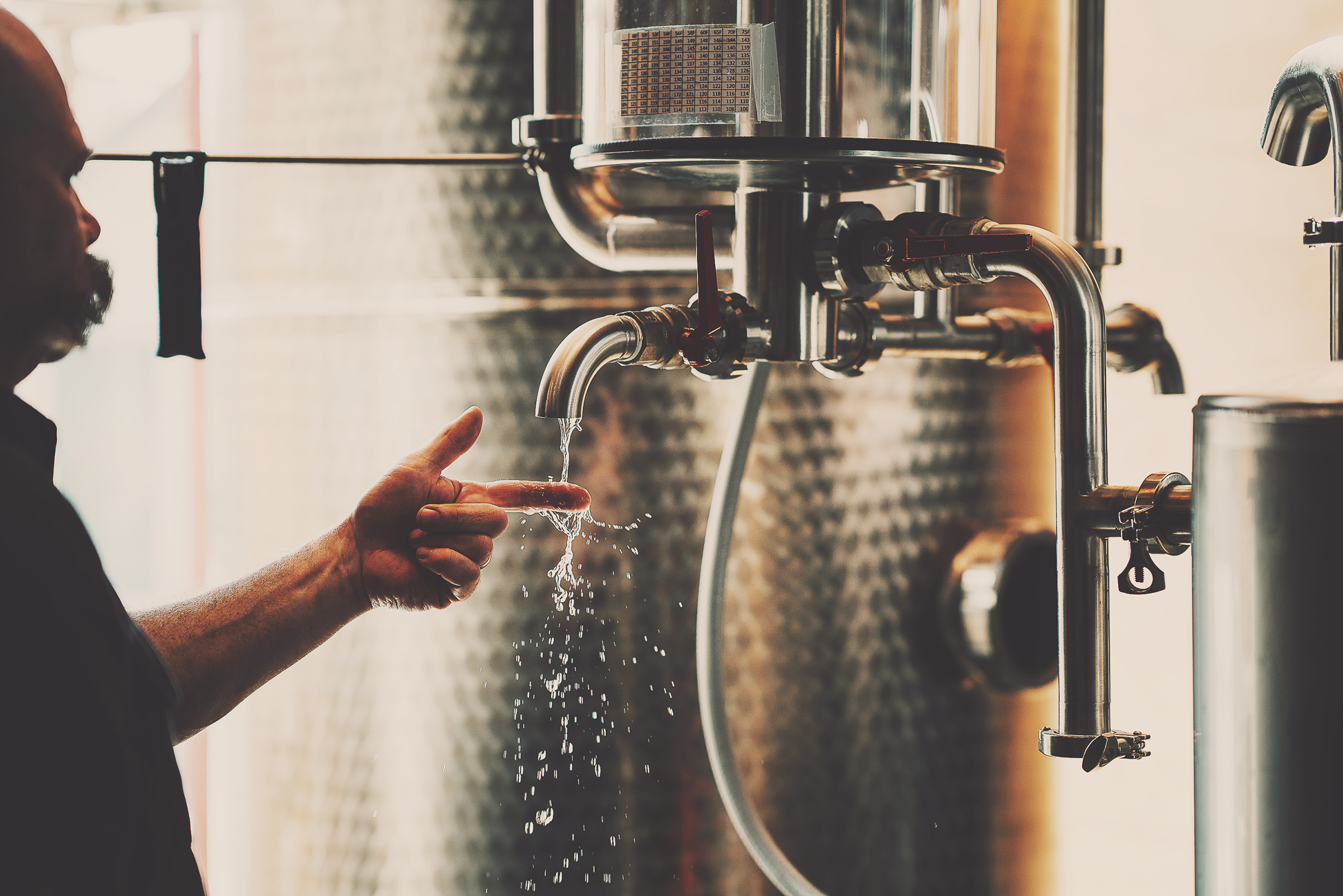 Person interacting with industrial equipment in a brewing or distilling setting.