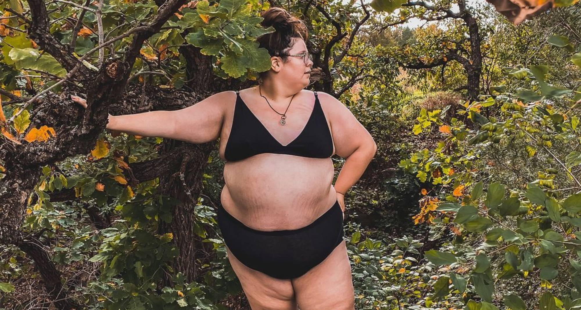 A woman wears size inclusive brand WAMA Underwear standing amongst the autumn leaves. 