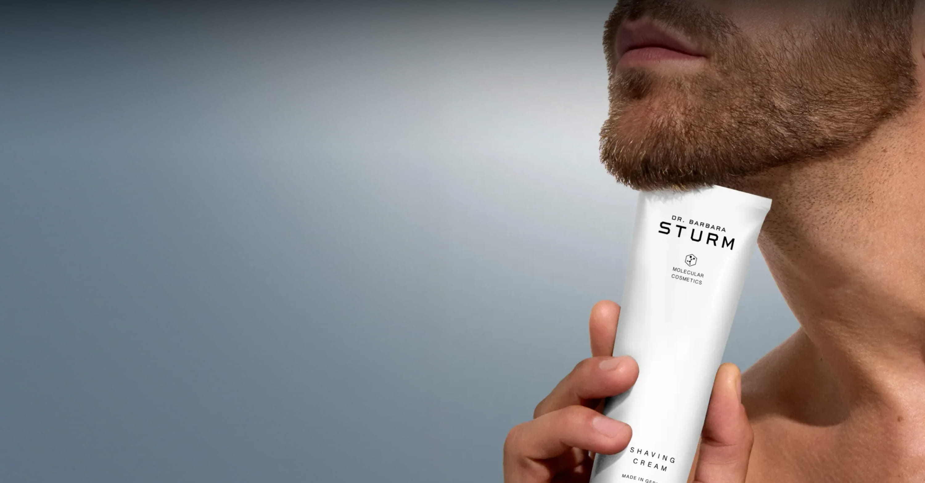 A man holding a skincare product near his chin against a blurred background.