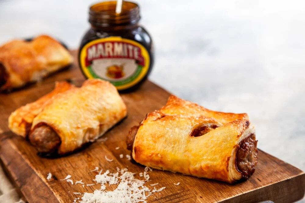 Marmite and cheese sausage rolls on a chopping board.