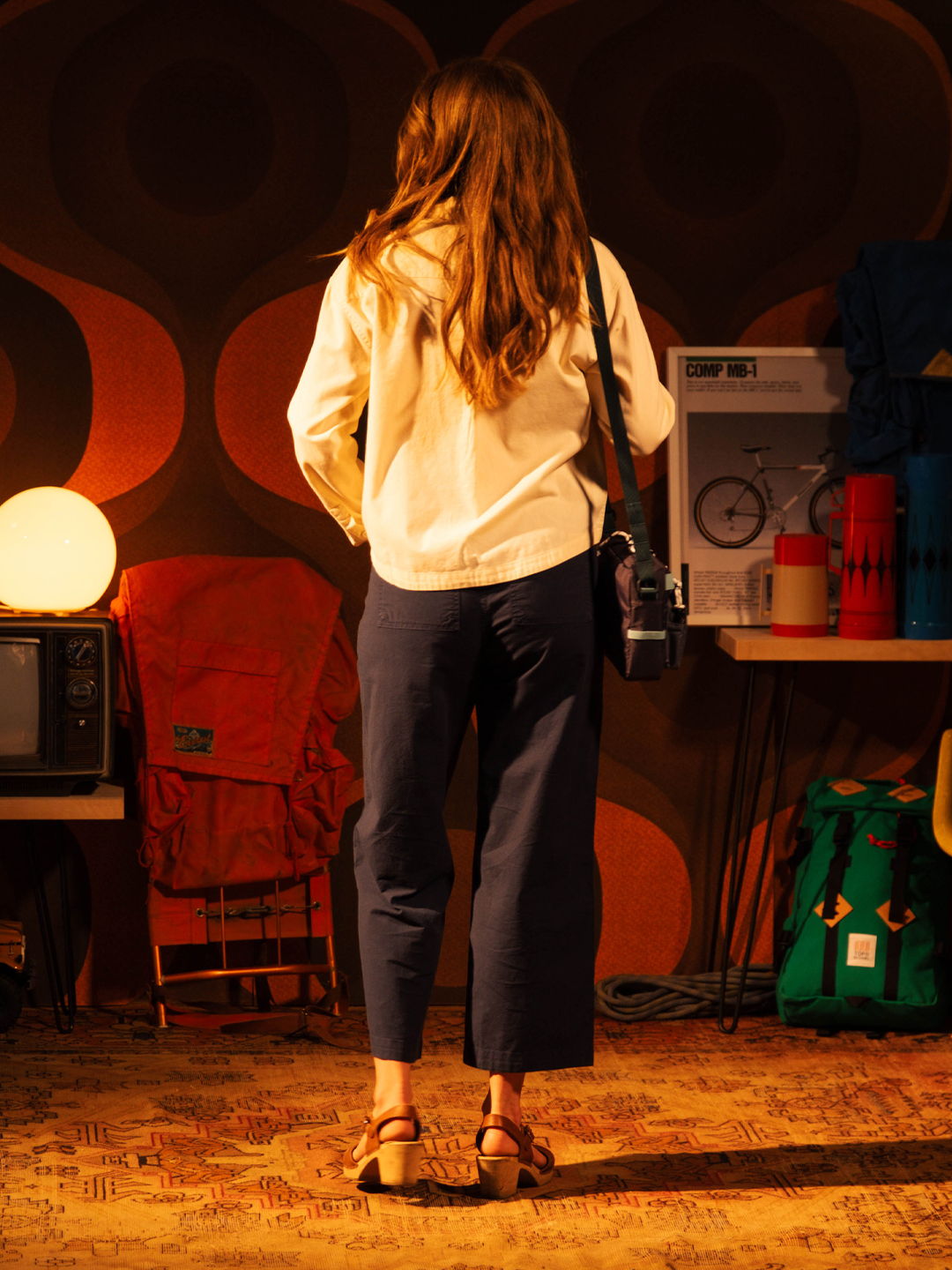 Person with long hair wearing casual clothes, standing in a retro-themed room.
