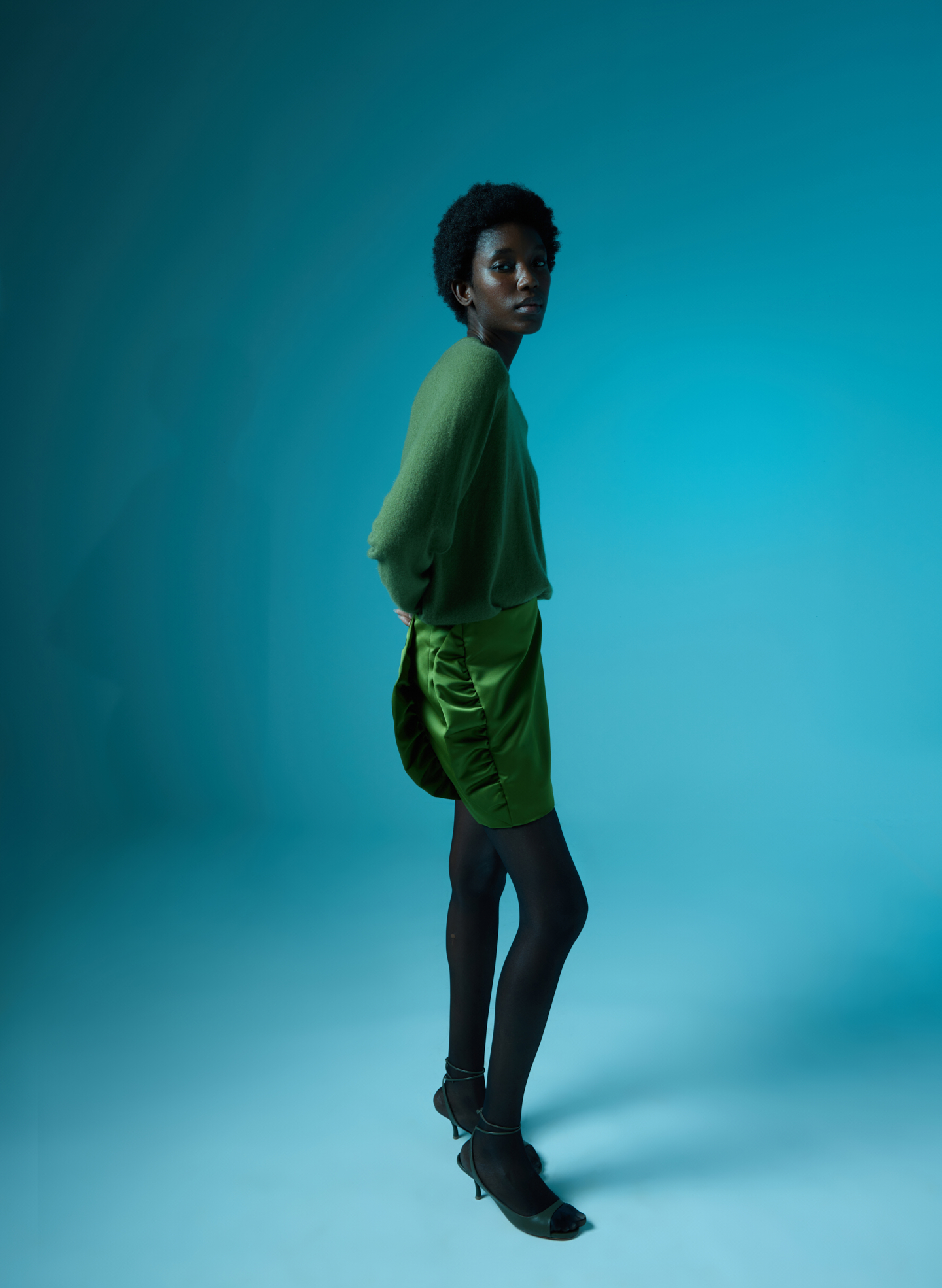 Person in green attire against a blue background, standing sideways.