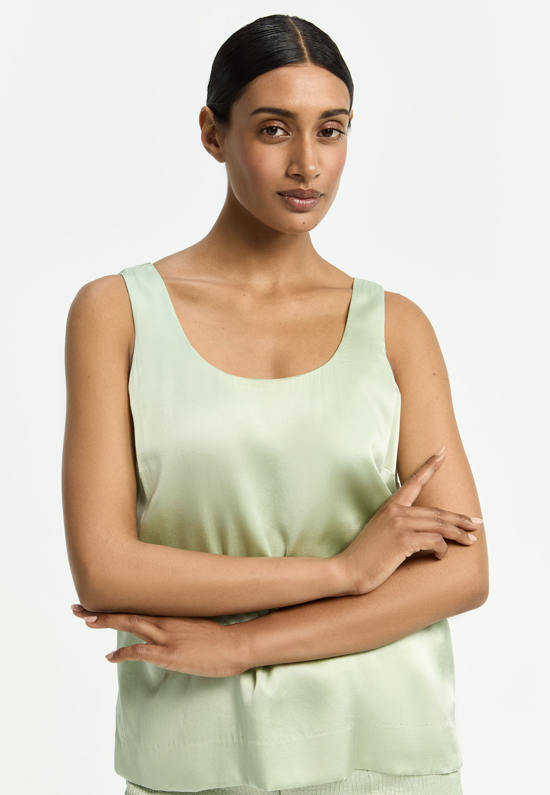 A model poses in a light green satin tank top.