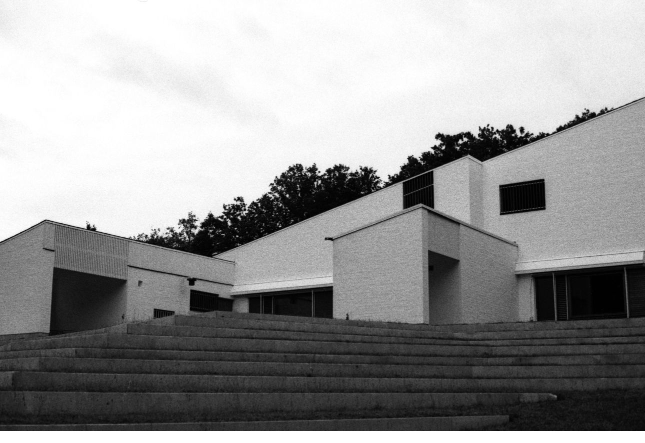 Modern architectural building with stairs, trees in background, black and white.
