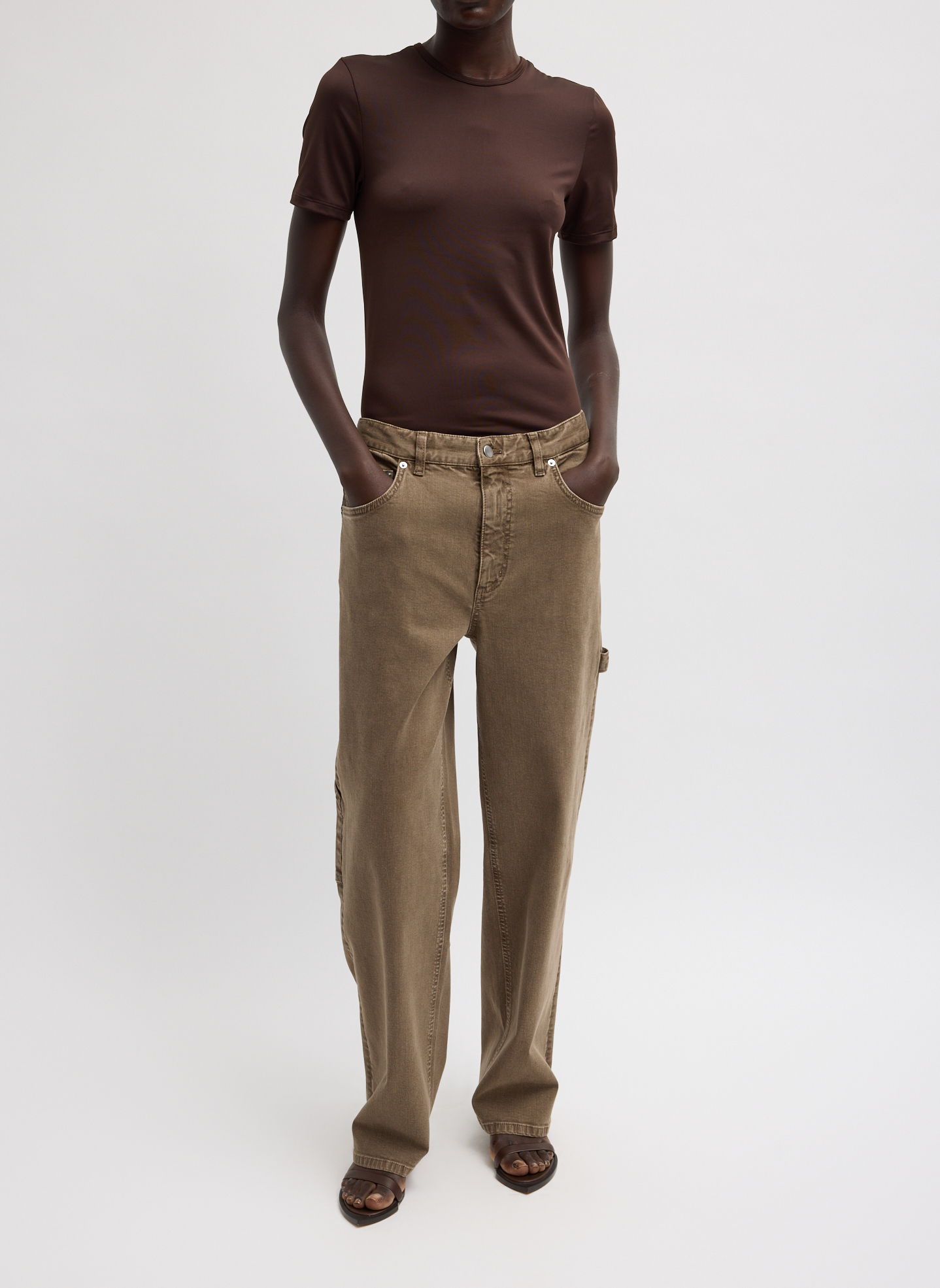 A person wearing a brown shirt and khaki pants, standing with hands in pockets.