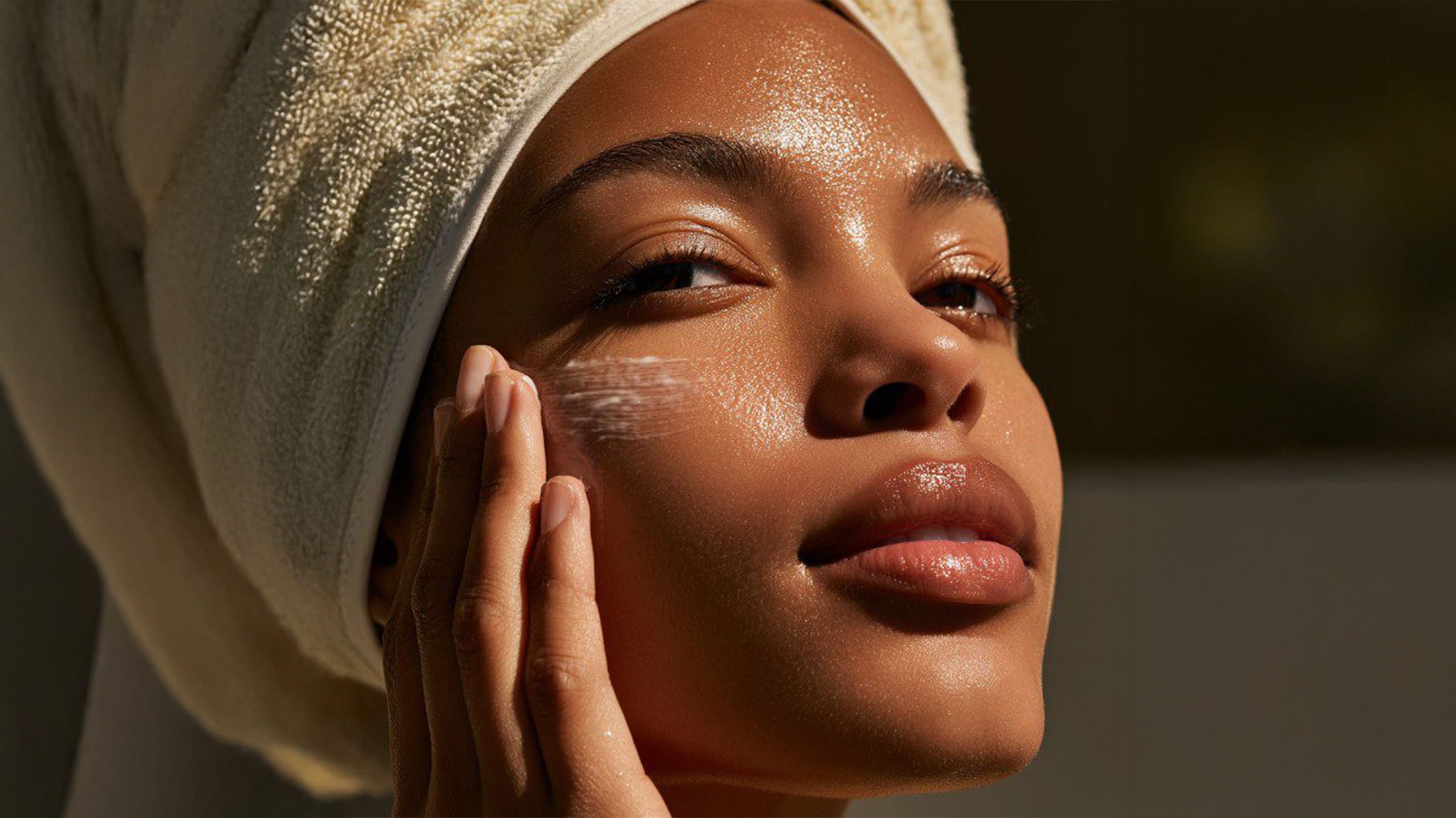 Person with glowing skin touching their face, wearing a towel on their head.
