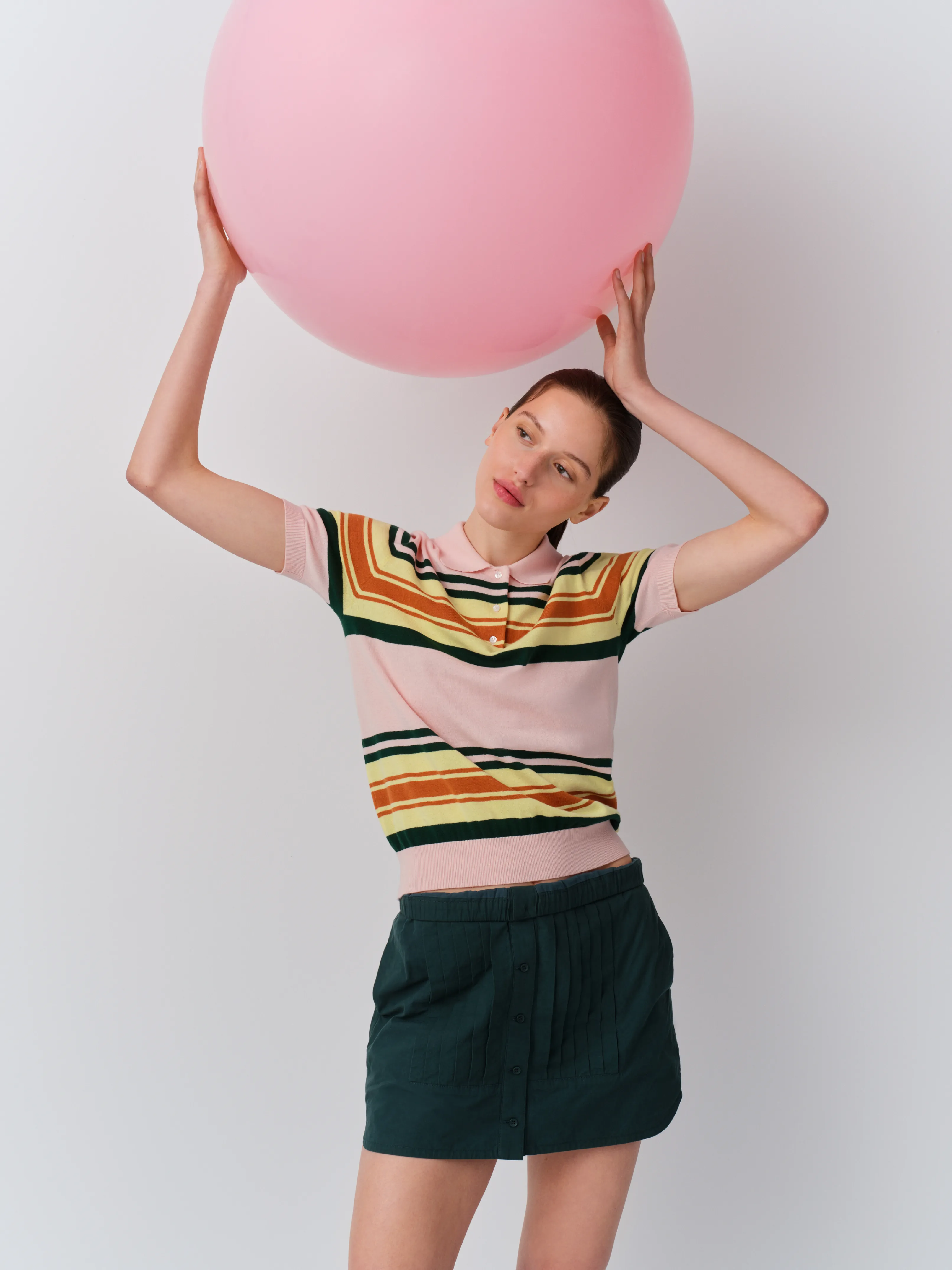 Woman holding a large pink balloon, wearing a colorful striped shirt and shorts.