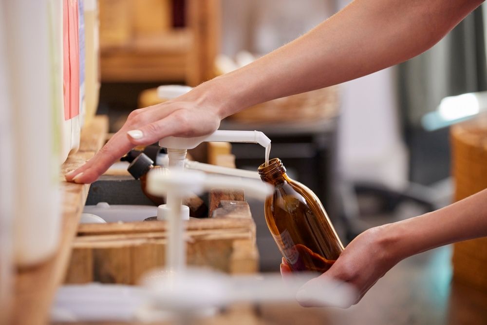 A person filling a bottle from a dispenser in a shop.