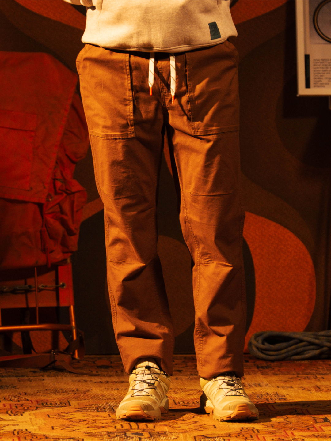 Person wearing brown pants and white sneakers on a patterned floor.