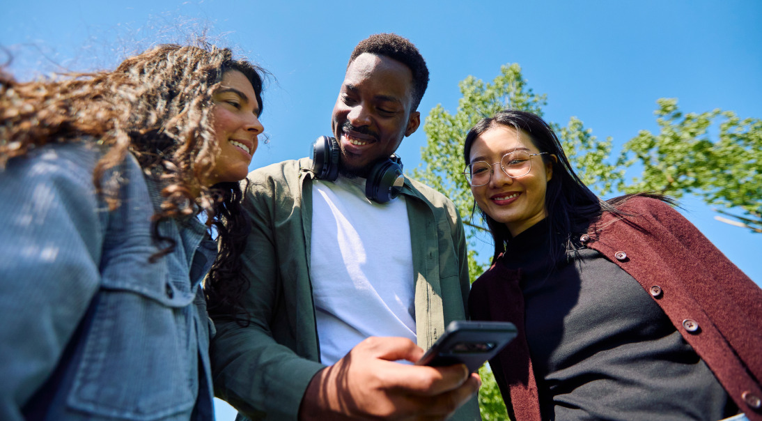 Three friends looking at a smartphone outdoors on a sunny day.