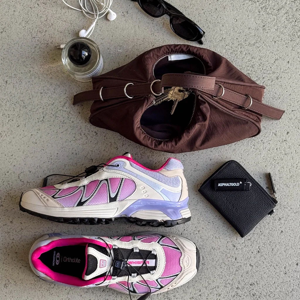 A pair of pink and white sneakers next to a brown bag and accessories.