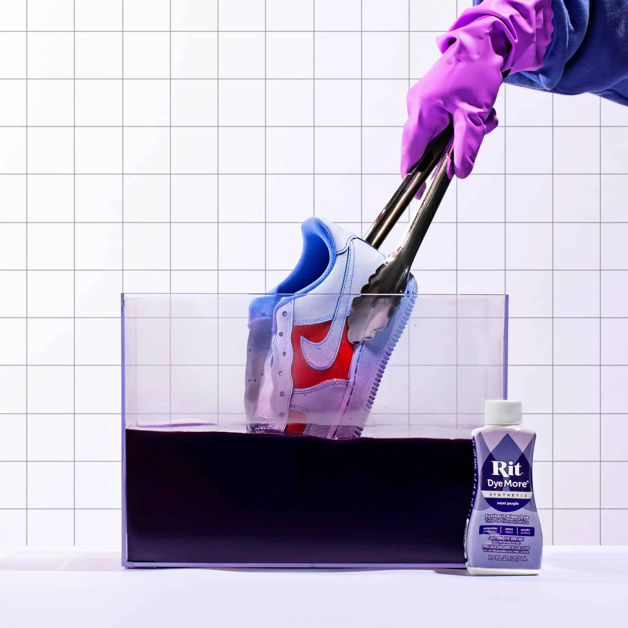 A sneaker being cleaned in a solution with gloved hands.