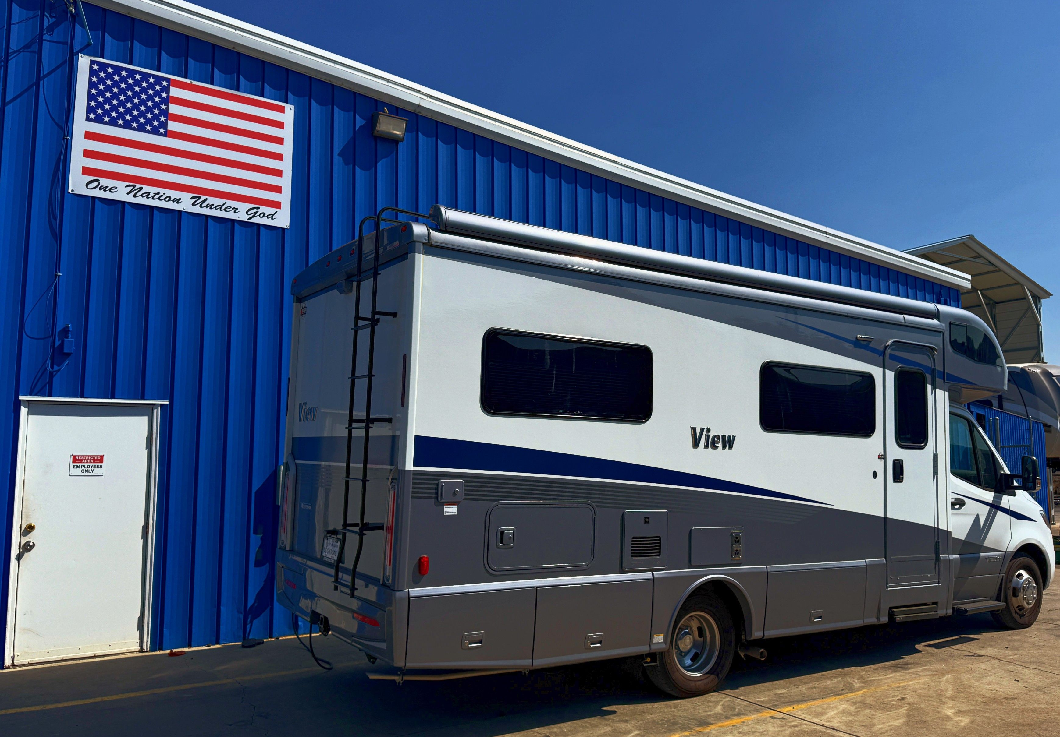 A camper van parked next to a blue building with an American flag.