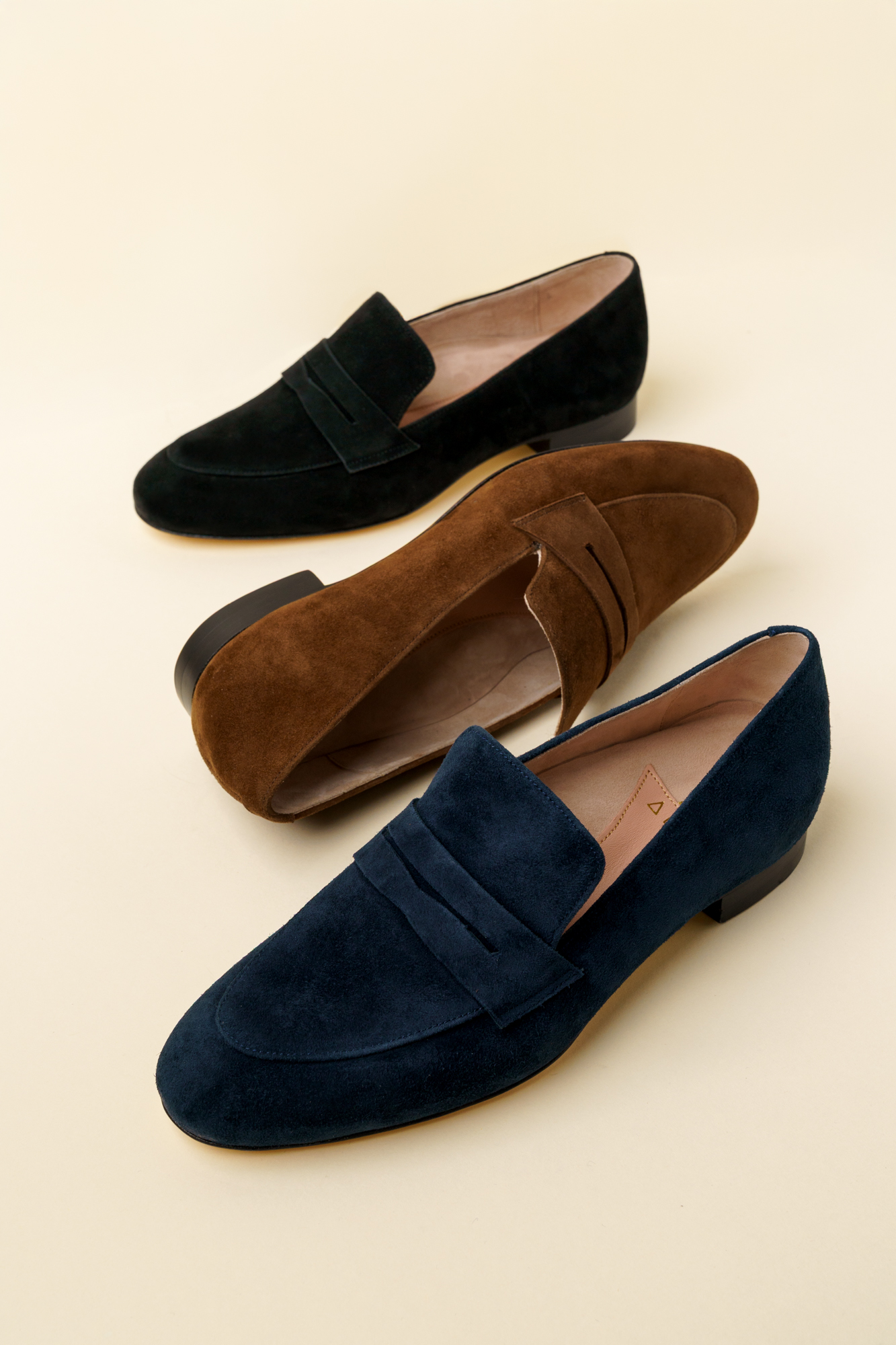 Three pairs of stylish suede loafers in black, brown, and navy.