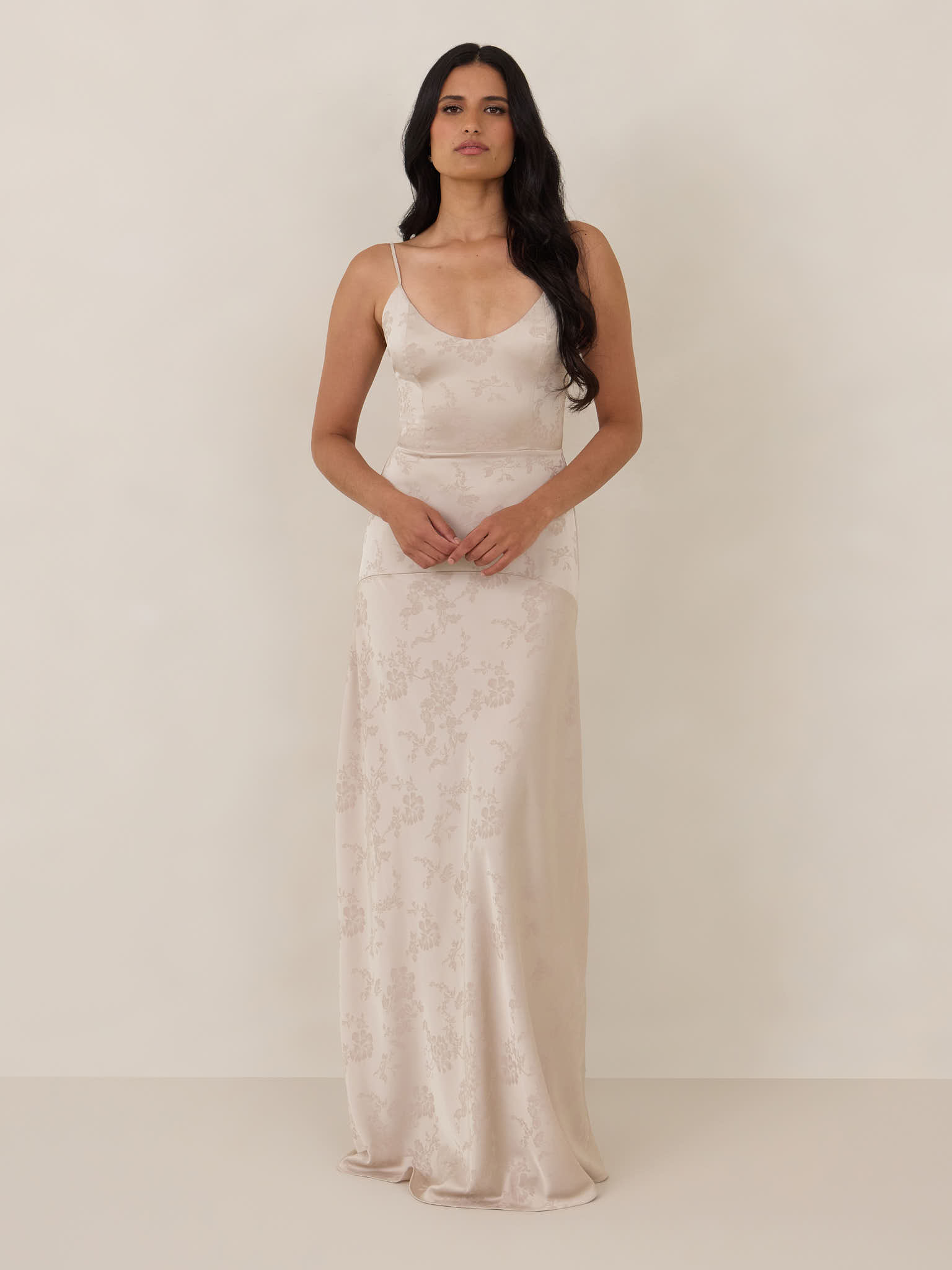 Woman in a sleek, light-colored dress standing against a neutral background.