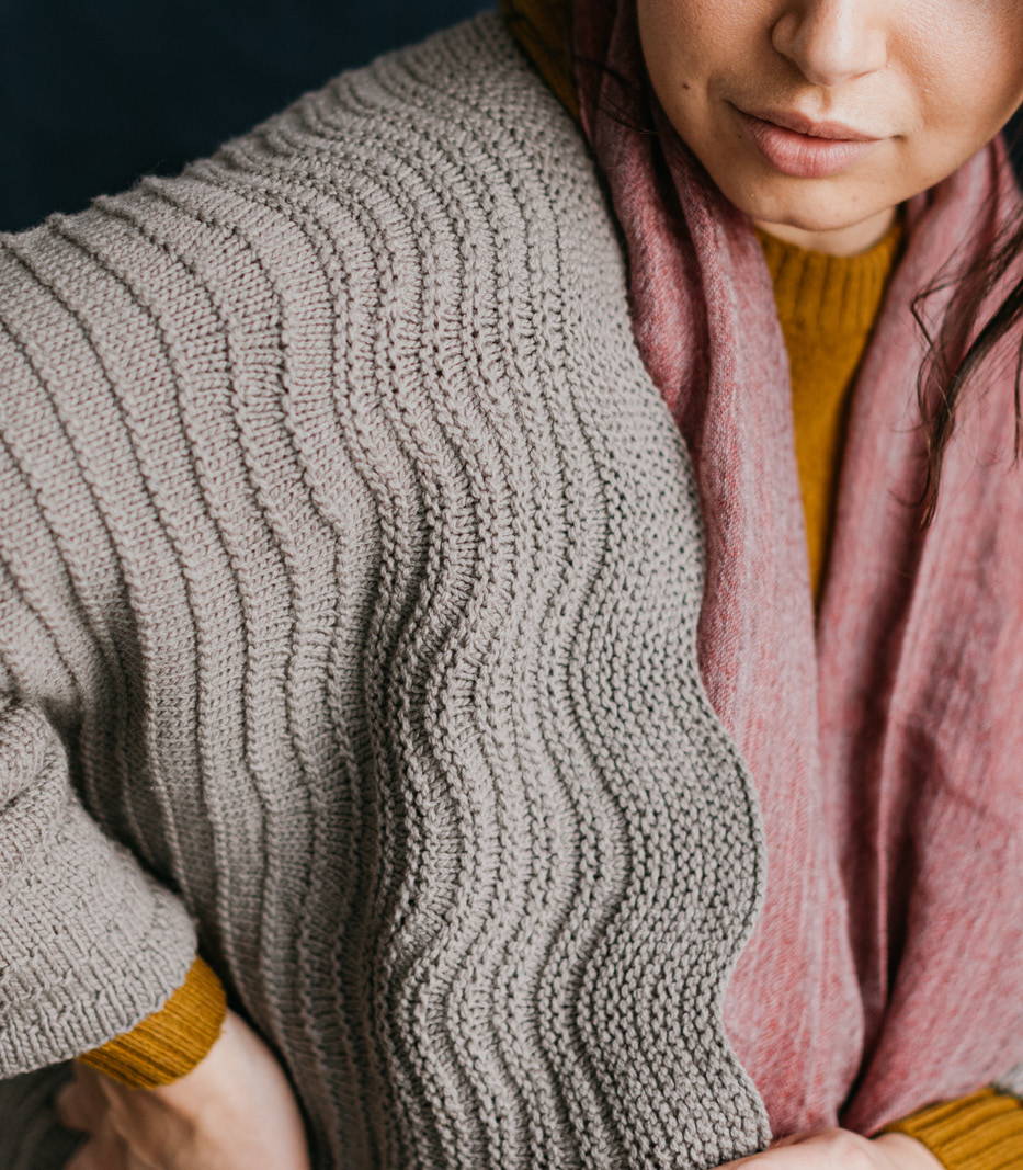 Closeup shot of a woman modelling a hand knit sideways textured cardigan in wool yarn.