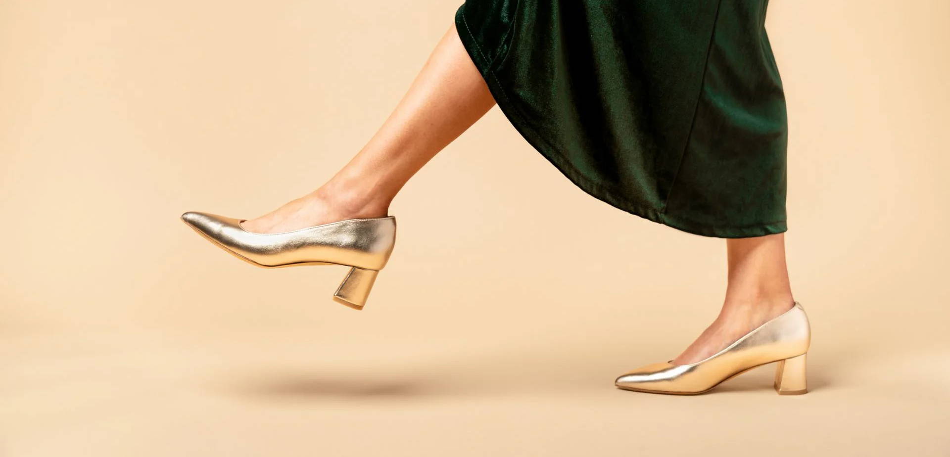 A person wearing silver heels and a green dress, stepping forward.
