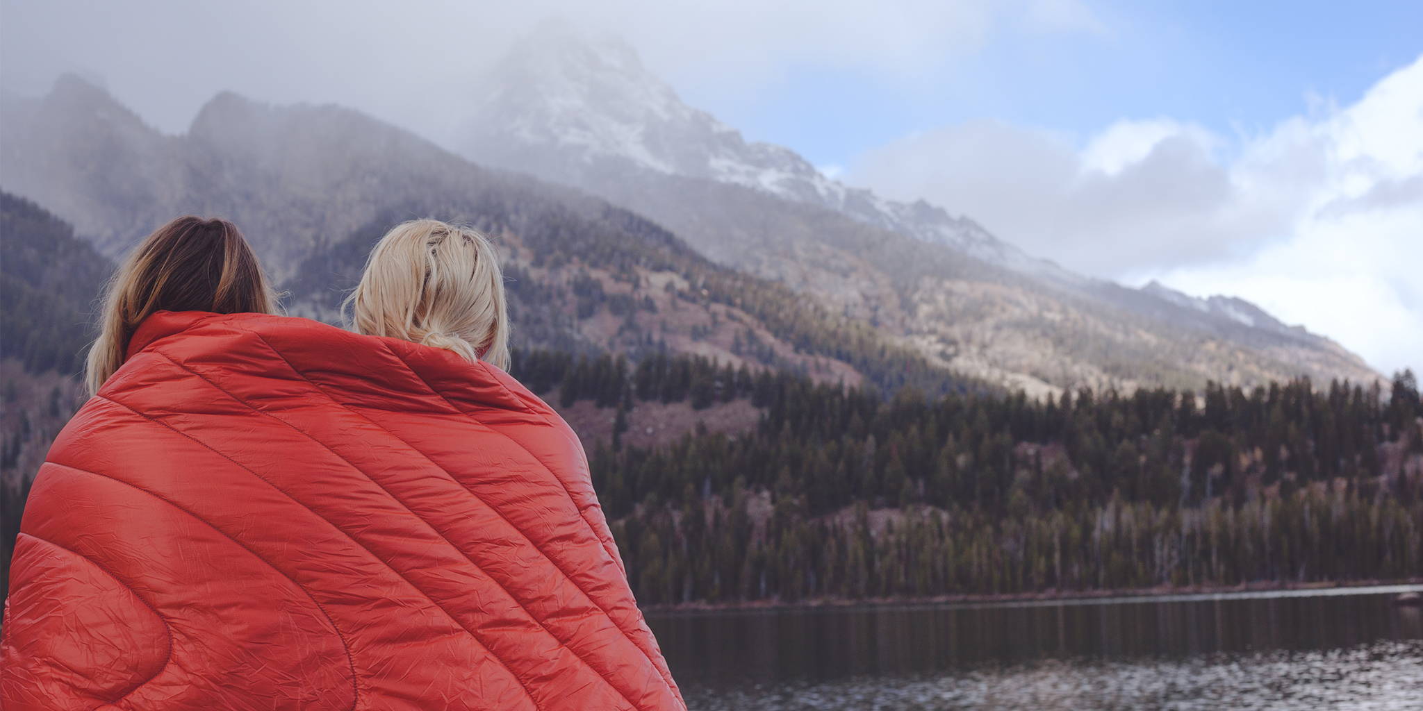 Two women staring at a mountain lake under a Rumpl puffy blanket