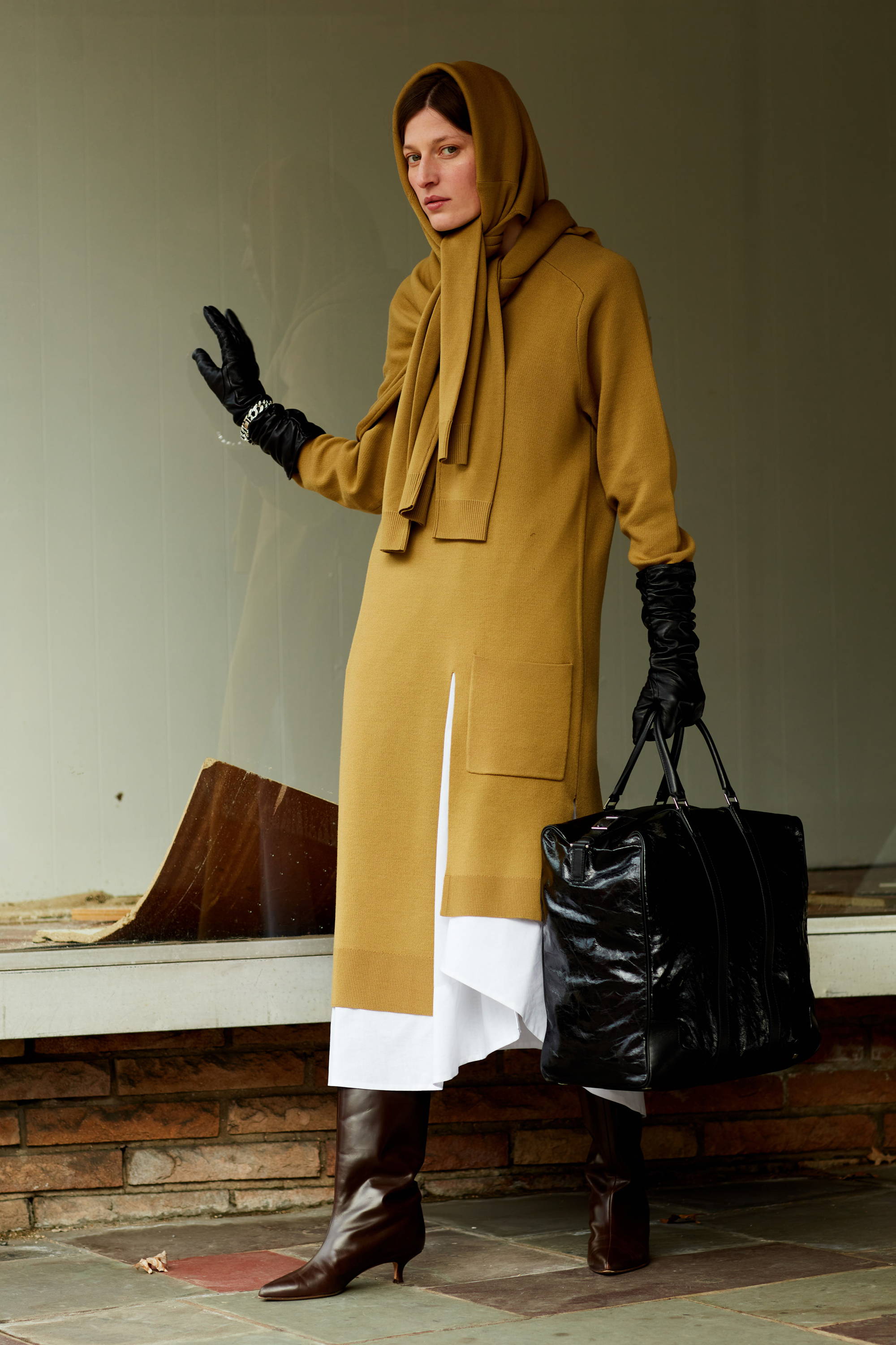 Model in stylish outfit with gloves and a handbag, posing confidently.