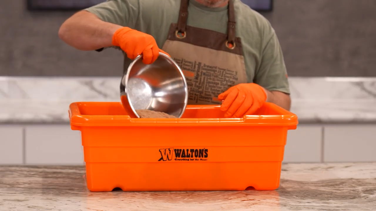 Person wearing gloves pouring contents from a bowl into an orange container.
