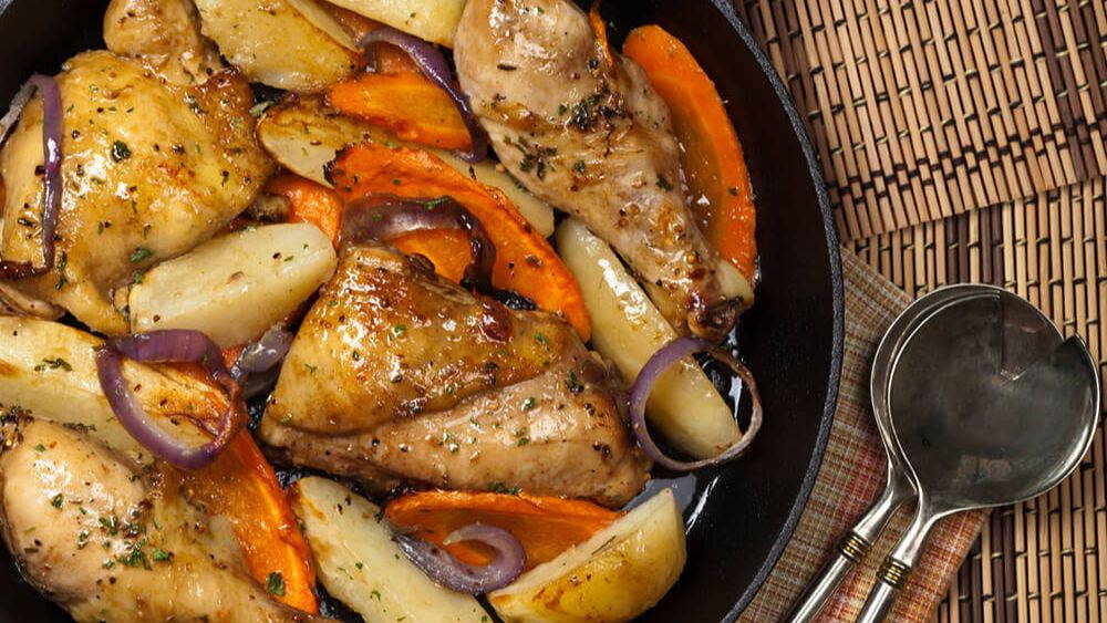 glazed chicken pieces in a cast iron with shiny carrots and potatoes