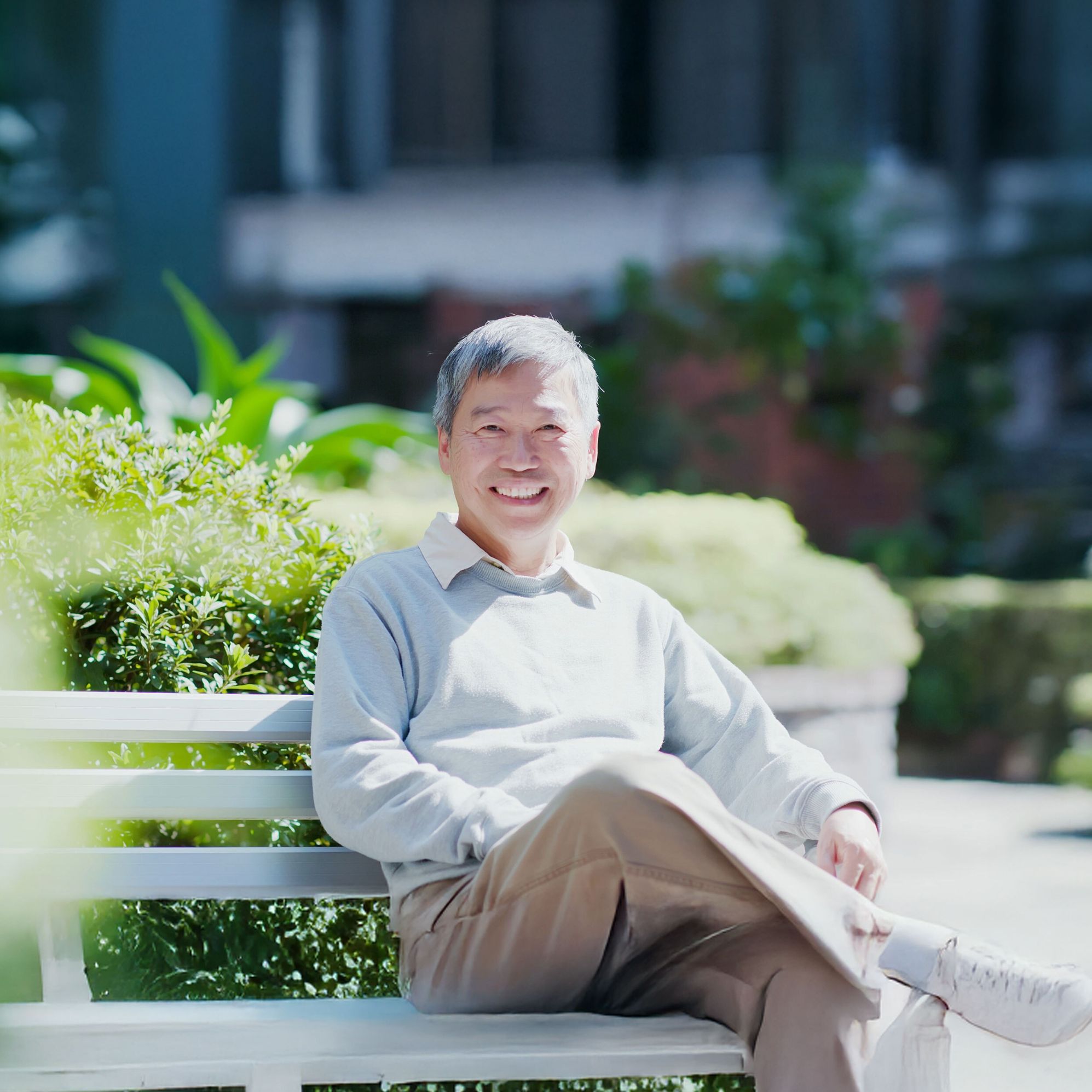 Smiling elderly man sitting on a bench in a sunny park.