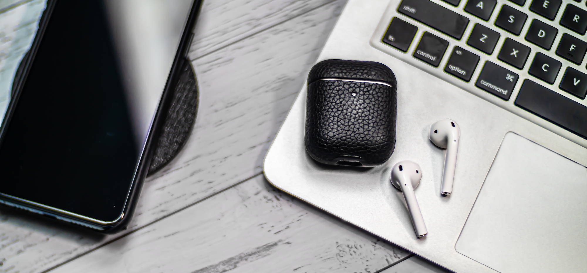 black genuine leather airpods case laying flat on a macbook air and wooden table